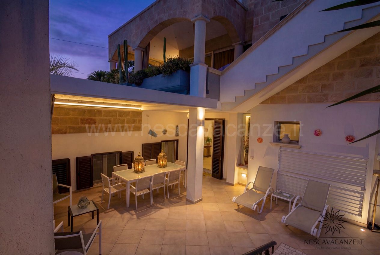 Casa Pescoluse 2 - patio al crepuscolo con tavolo, lanterne accese, lettini e scala esterna