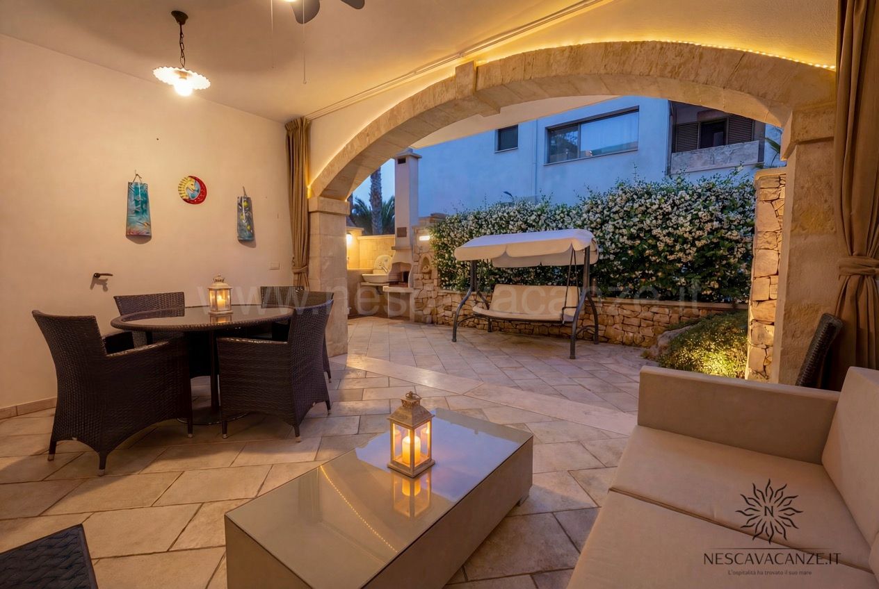 Casa Pescoluse 6 - veranda coperta al tramonto con salotto in rattan, divano e lanterne accese