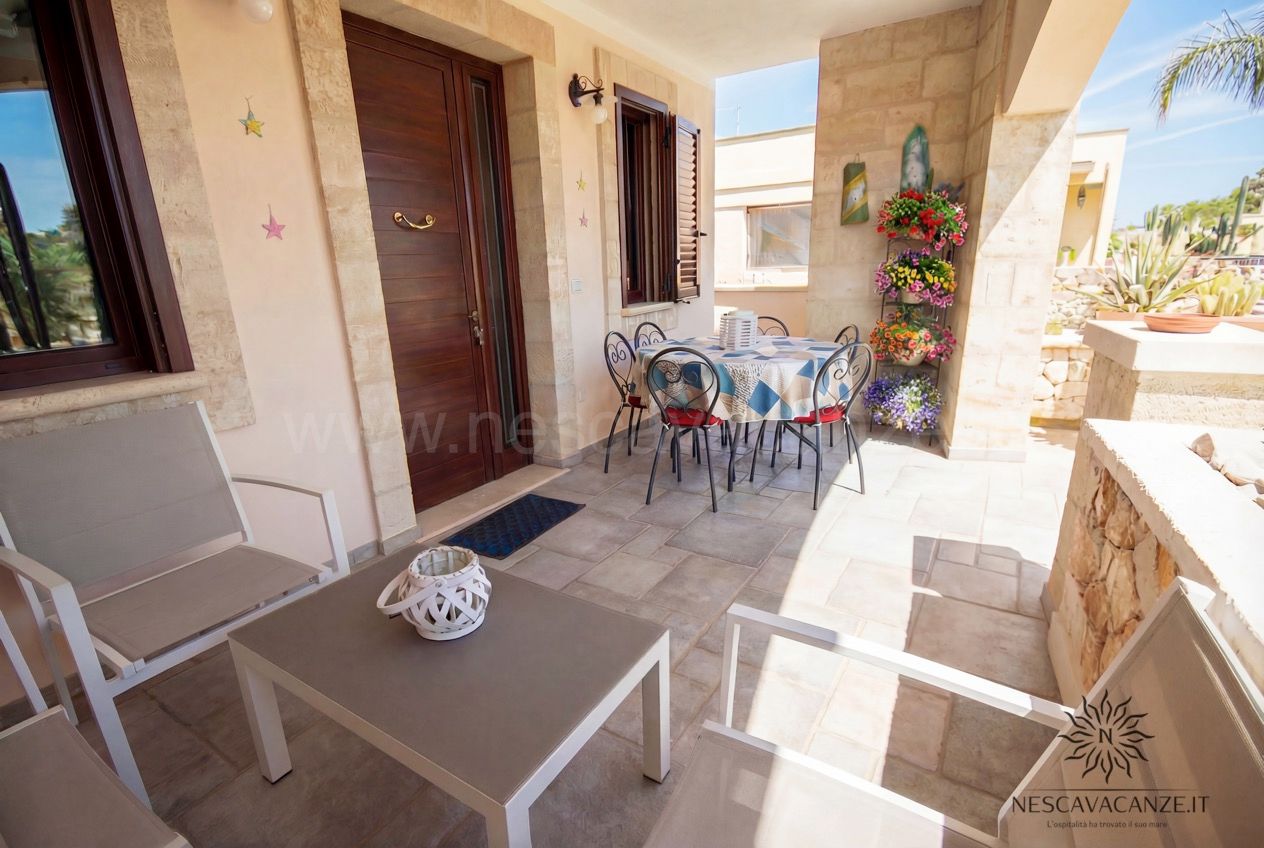 Casa Pescoluse 4 - veranda d'ingresso con porta in legno, tavolo e sedie, poltrone e fioriera