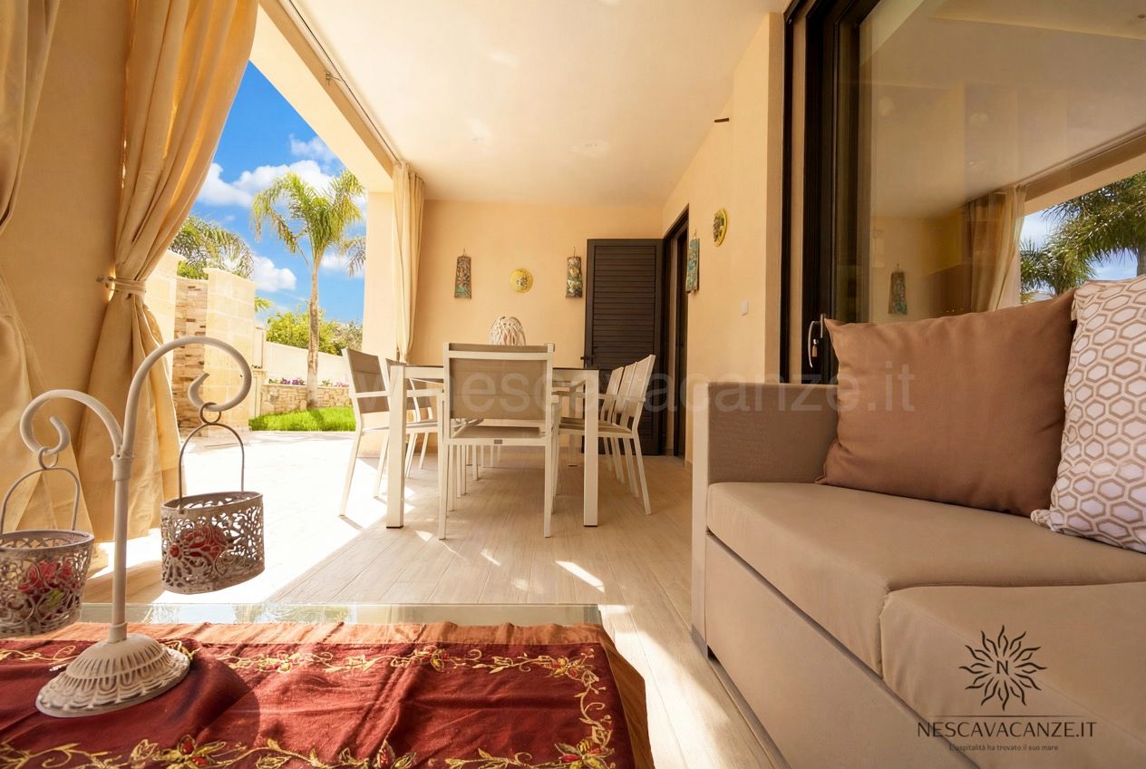Casa Salento - veranda con tavolo e sedie bianche, divano e tende, vista sul giardino con palma
