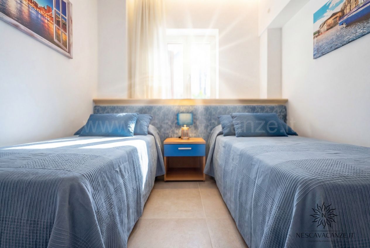 Casa Pescoluse 2 - camera con due letti singoli azzurri, comodino centrale e finestra luminosa