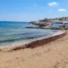 La spiaggetta libera di sabbia sul lungomare di Santa Maria di Leuca, con il mare calmo e le case bianche