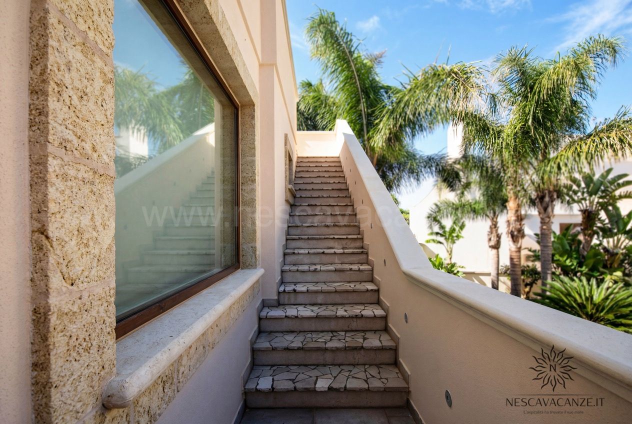 Casa Pescoluse 4 - scala esterna in pietra con grande vetrata, palme e cielo azzurro