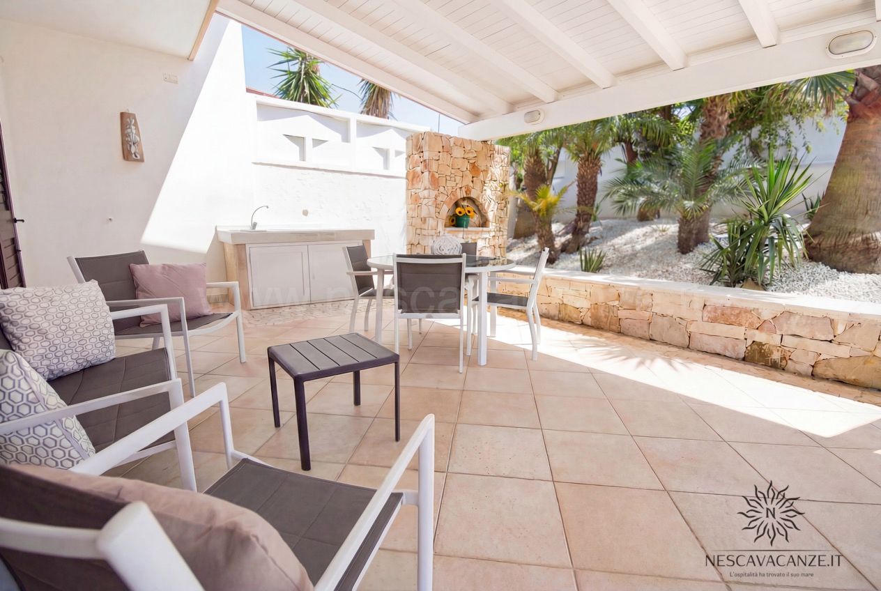 Casa Pescoluse 3 - patio coperto con poltrone imbottite, tavolo in vetro, lavabo esterno e barbecue in pietra