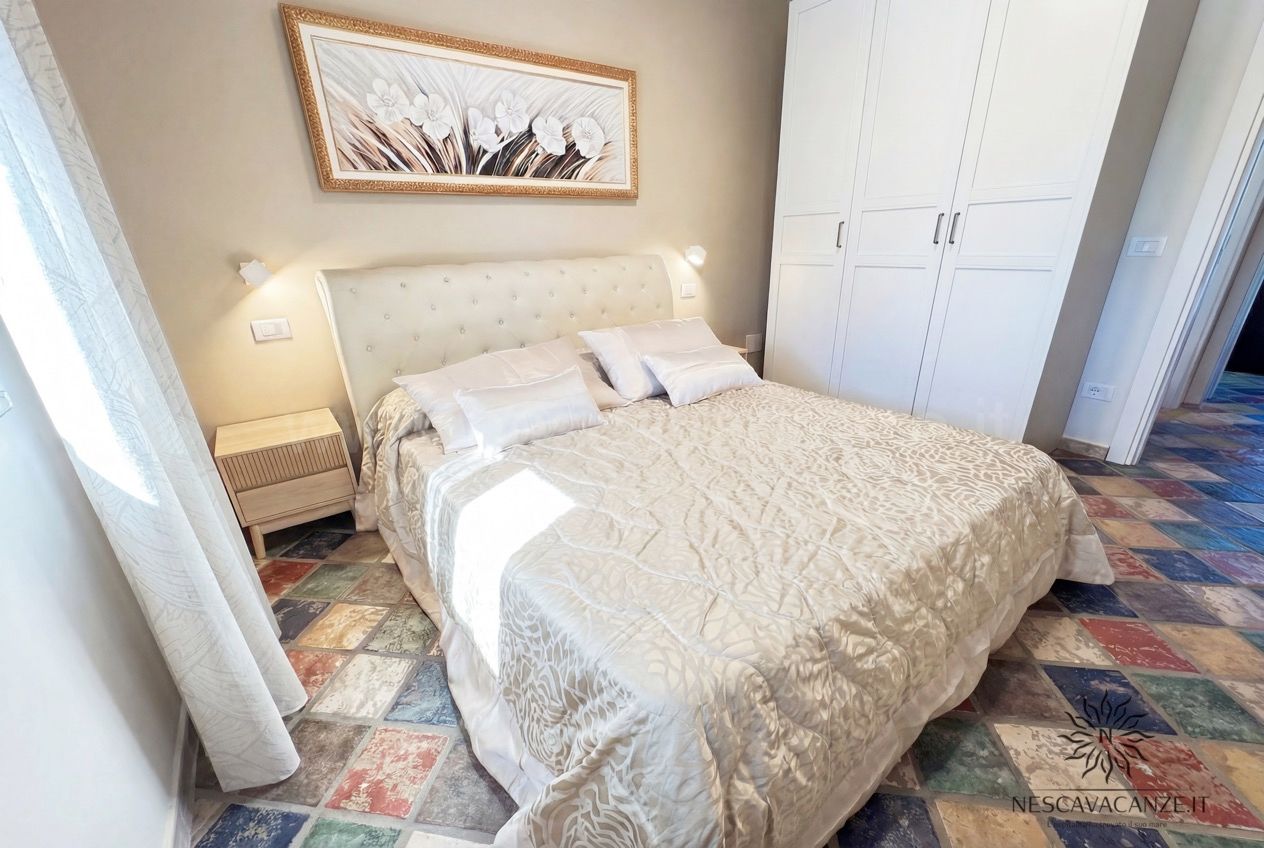 Casa Sabbia Oro - camera matrimoniale con testiera capitonné, armadio bianco e quadro floreale