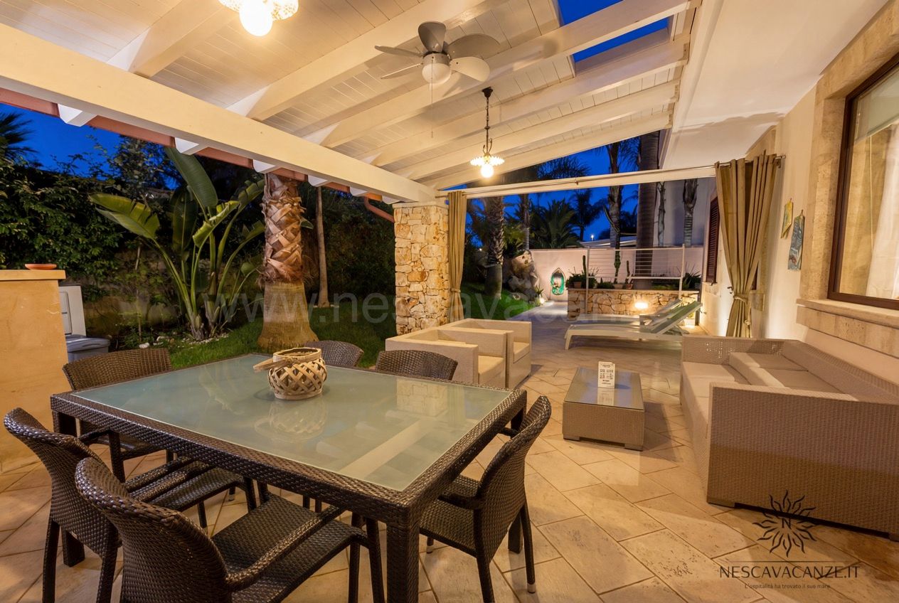 Casa Pescoluse 7 - terrazza coperta con tavolo e divani al crepuscolo tra le palme