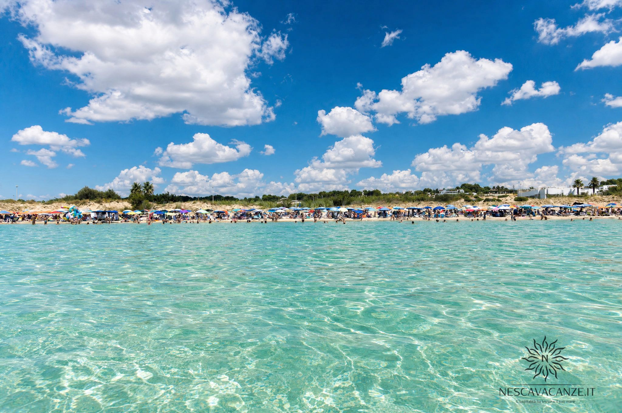 Maldive del Salento - Spiaggia affollata vista dall'acqua, bagnanti sotto ombrelloni colorati su sabbia chiara