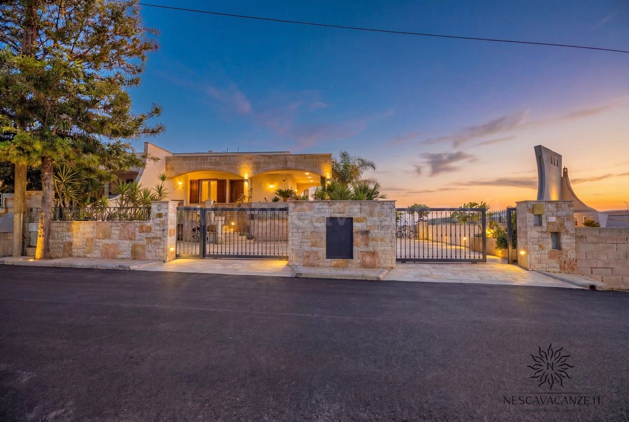 Casa Pescoluse 2 - facciata della villa illuminata al tramonto con cancello e muro in pietra