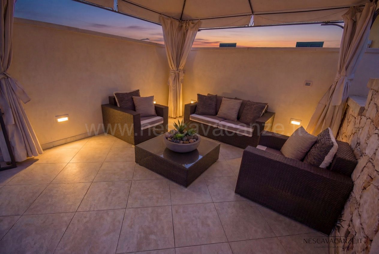 Casa Pescoluse 9 - terrazza lounge al tramonto con divani in rattan, gazebo e luci soffuse