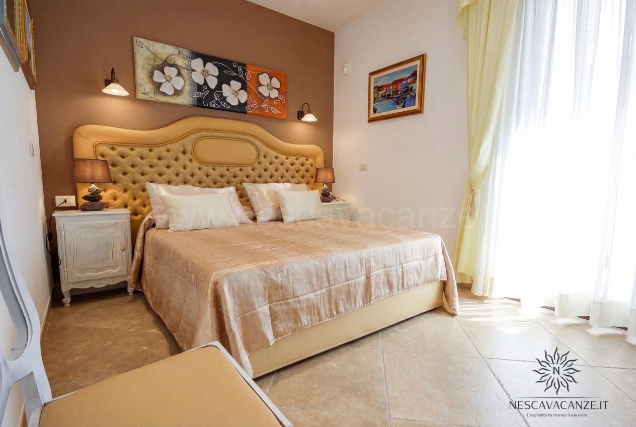 Casa Pescoluse 9 - camera matrimoniale con parete color tortora, quadro floreale e tende gialle