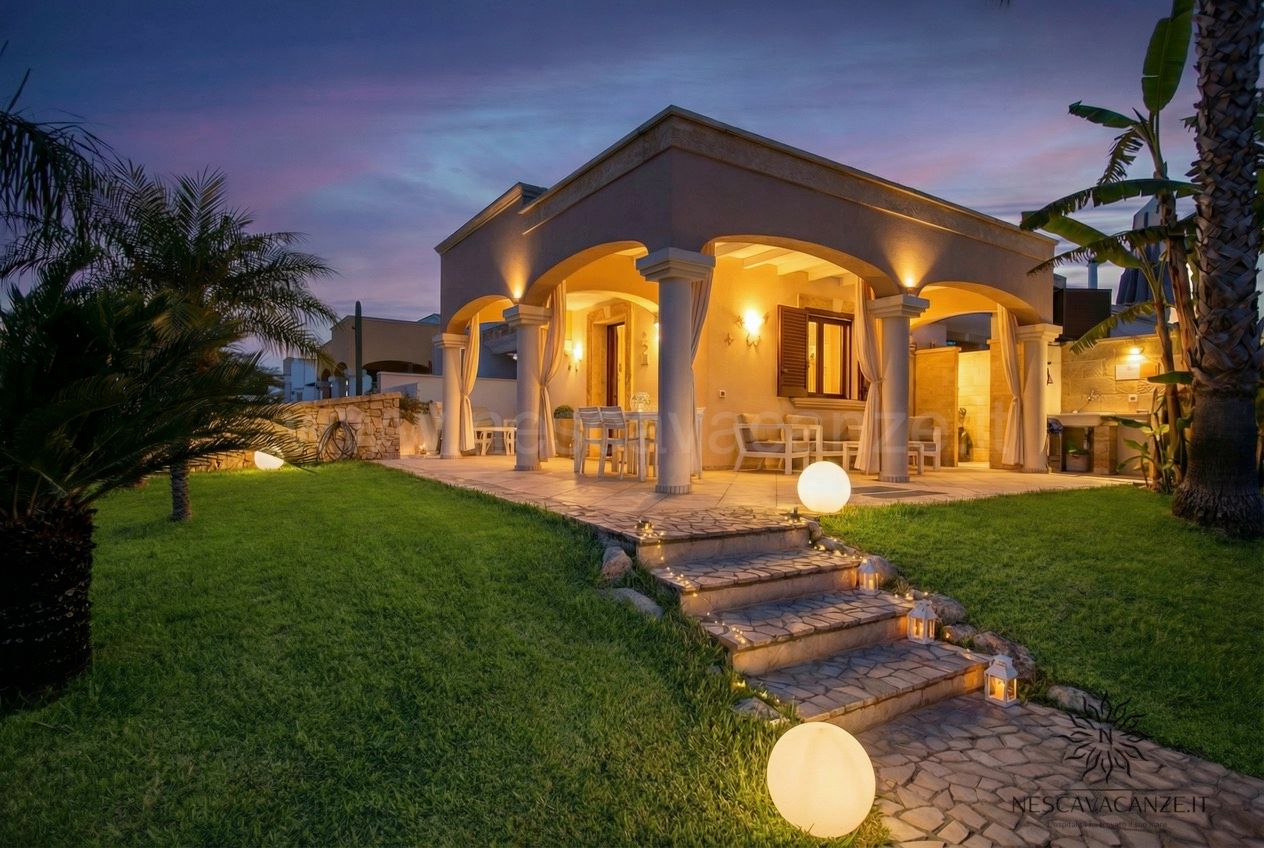 Casa Pescoluse 8 - Facciata della villa al tramonto con veranda illuminata e scalinata con lanterne