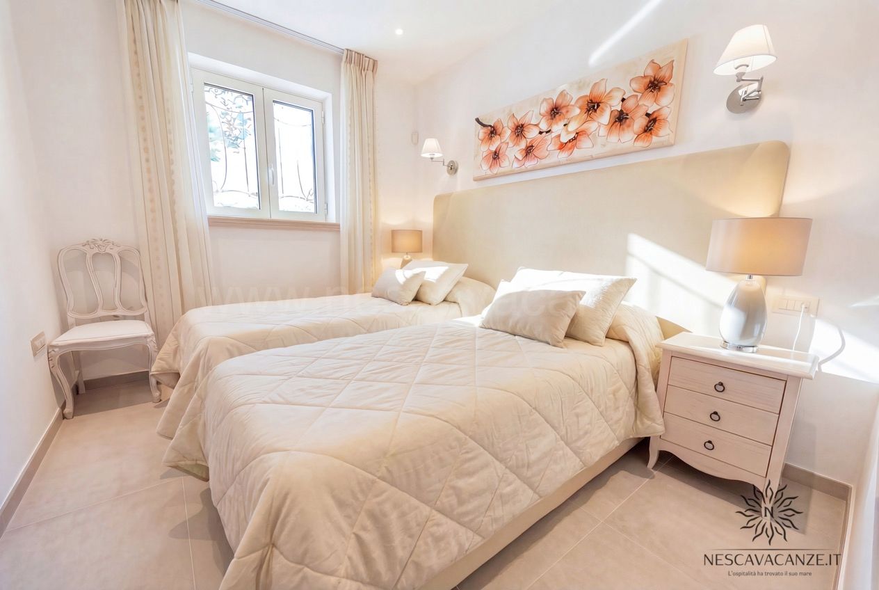 Casa Pescoluse 2 - camera con due letti, copriletto beige, quadro floreale e comodino chiaro