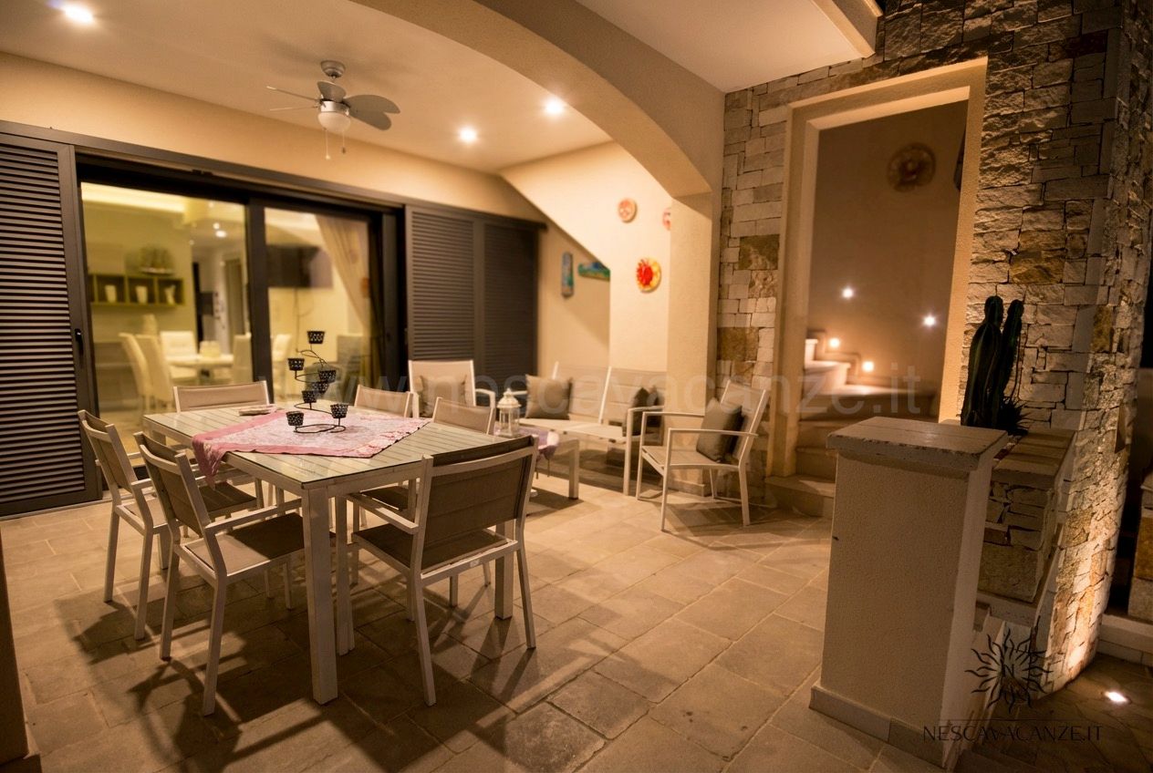 Casa Giglio - veranda illuminata di sera con tavolo, divani, ventilatore e parete in pietra