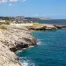 La costa rocciosa di Marina di Andrano verso nord, con il mare blu e il paese sullo sfondo