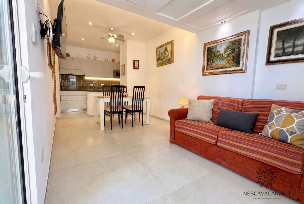 Casa Pescoluse 3 - soggiorno luminoso con divano rosso a righe, TV a parete, angolo cottura e tavolo da pranzo