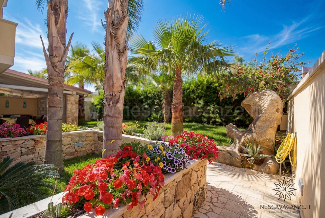 Casa Pescoluse 7 - giardino con palme, fioriere in pietra e petunie rosse e viola