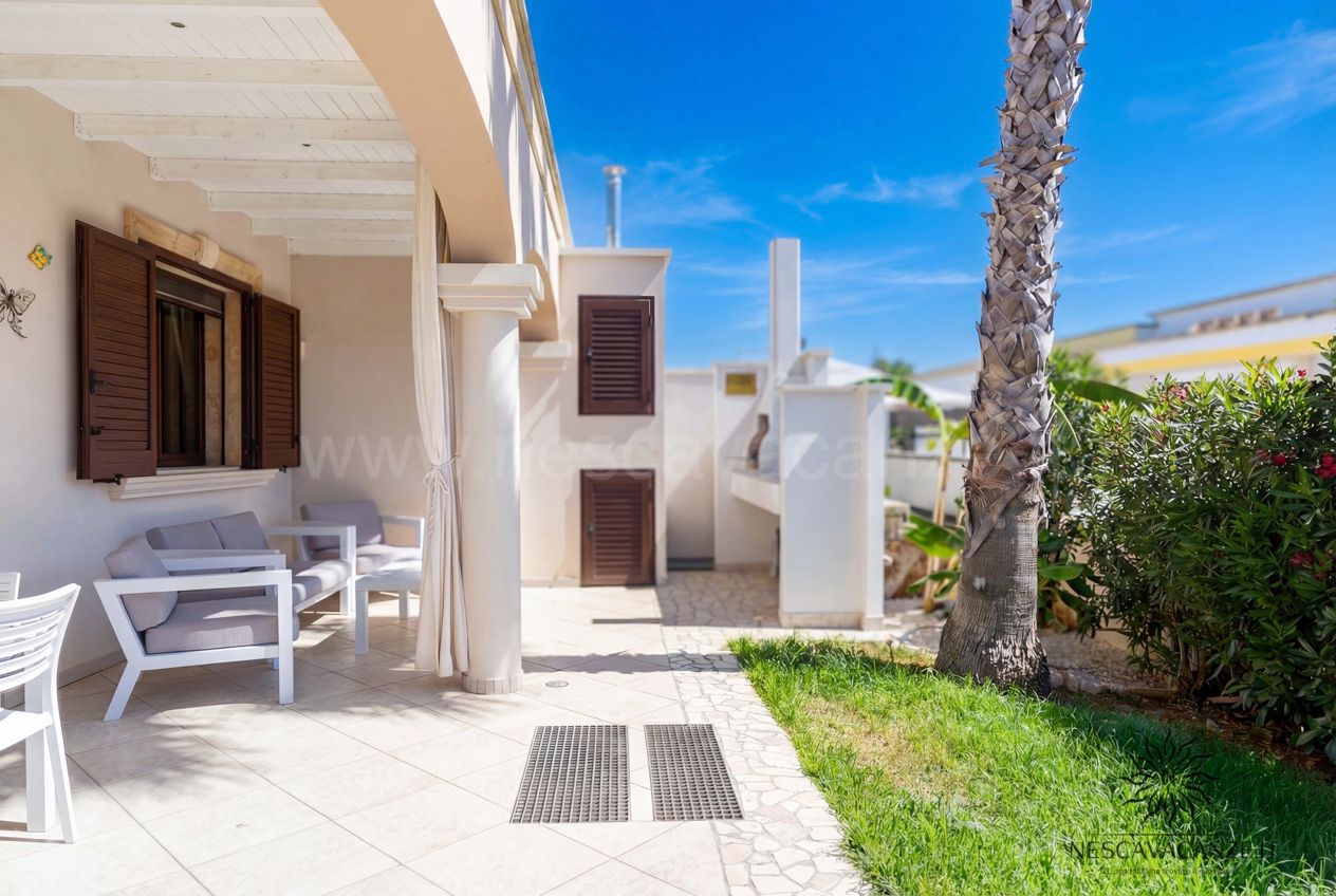 Casa Pescoluse 8 - Angolo veranda con divanetti bianchi, zona barbecue e palma nel giardino