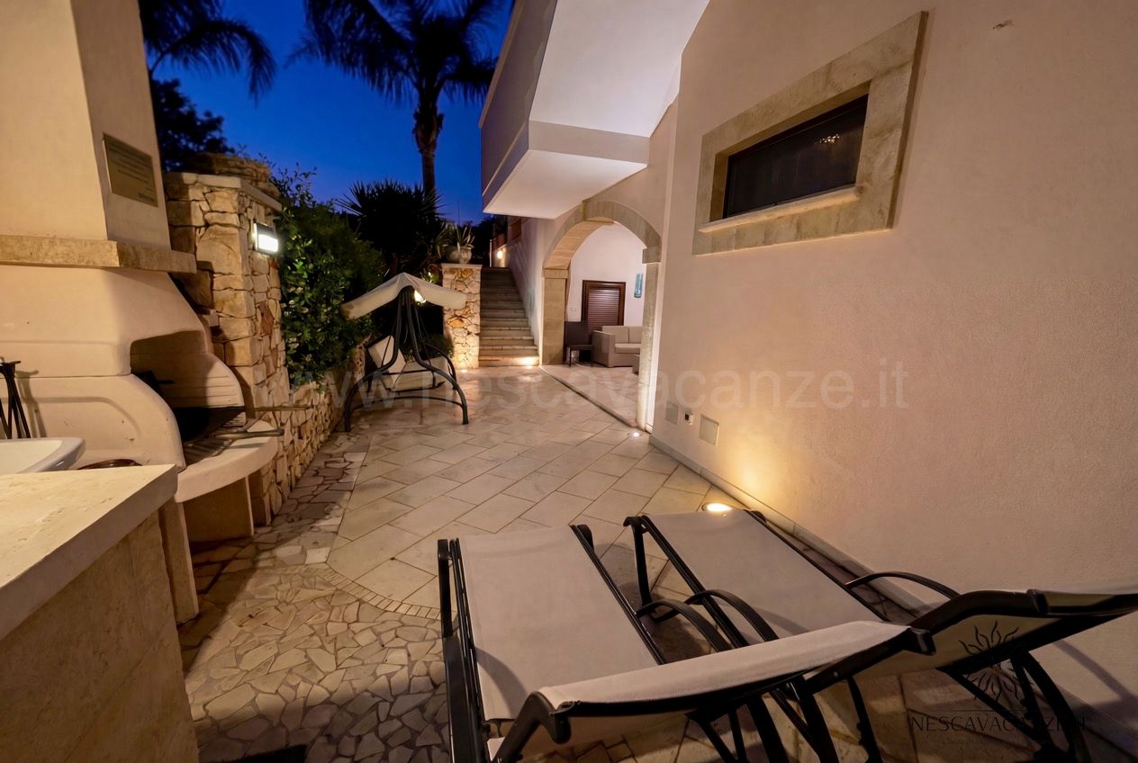 Casa Pescoluse 6 - patio al crepuscolo con lettini, cucina esterna e scala illuminata