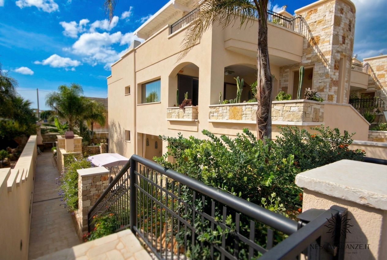 Casa Dune - esterno della villa beige con balconi e ringhiere nere, circondata dalla vegetazione rigogliosa