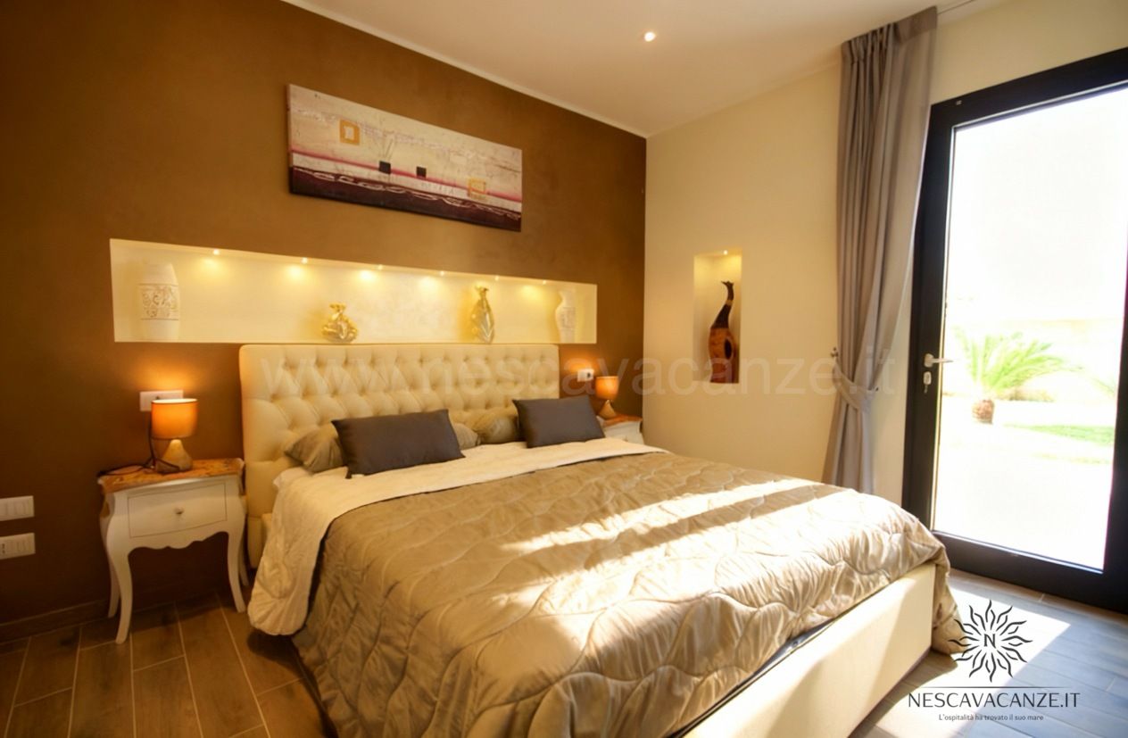 Casa Dune - camera da letto matrimoniale con testiera imbottita, copriletto color tortora e luce naturale dalla porta-finestr
