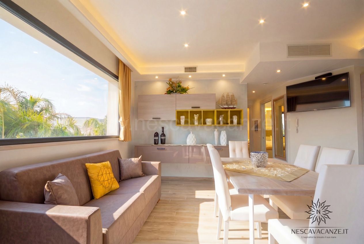Casa Giglio - soggiorno con divano, tavolo da pranzo, TV e grande finestra con vista palme