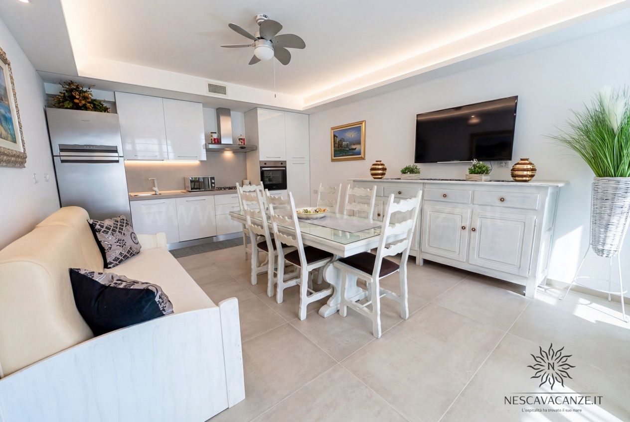 Casa Pescoluse 2 - zona giorno con cucina bianca, tavolo, divano, TV e frigo in acciaio