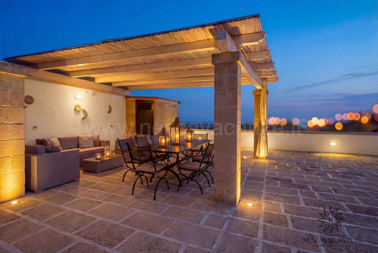 Casa Pescoluse 4 - terrazza al crepuscolo con pergolato illuminato, divano, tavolo e lanterne accese