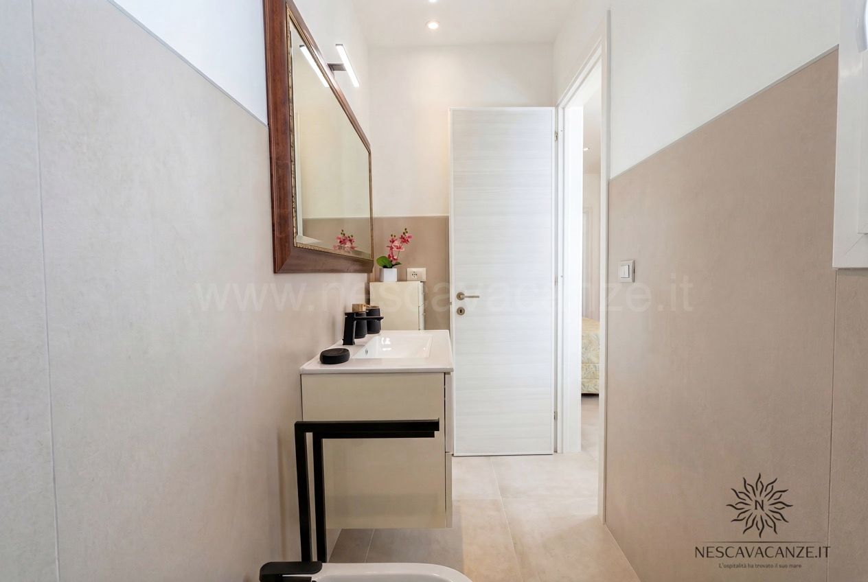 Casa Pescoluse 2 - bagno con mobile bianco, specchio in legno e corridoio verso la camera
