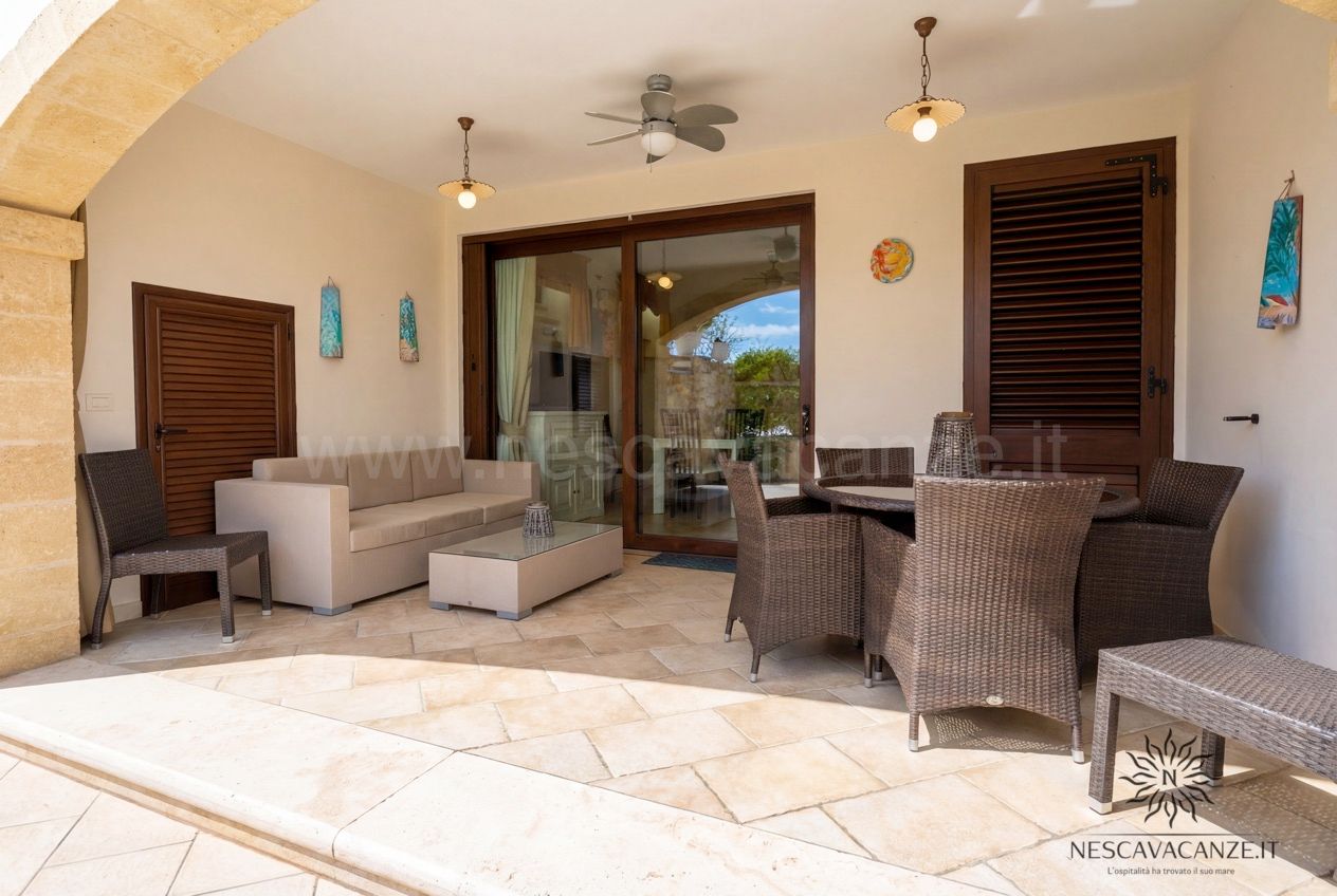 Casa Pescoluse 6 - veranda coperta con divano beige, salotto in rattan e tavolo in vetro