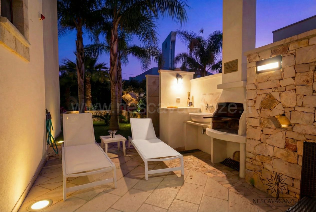 Casa Pescoluse 6 - lettini bianchi nel patio notturno con cucina esterna, lavabo e barbecue