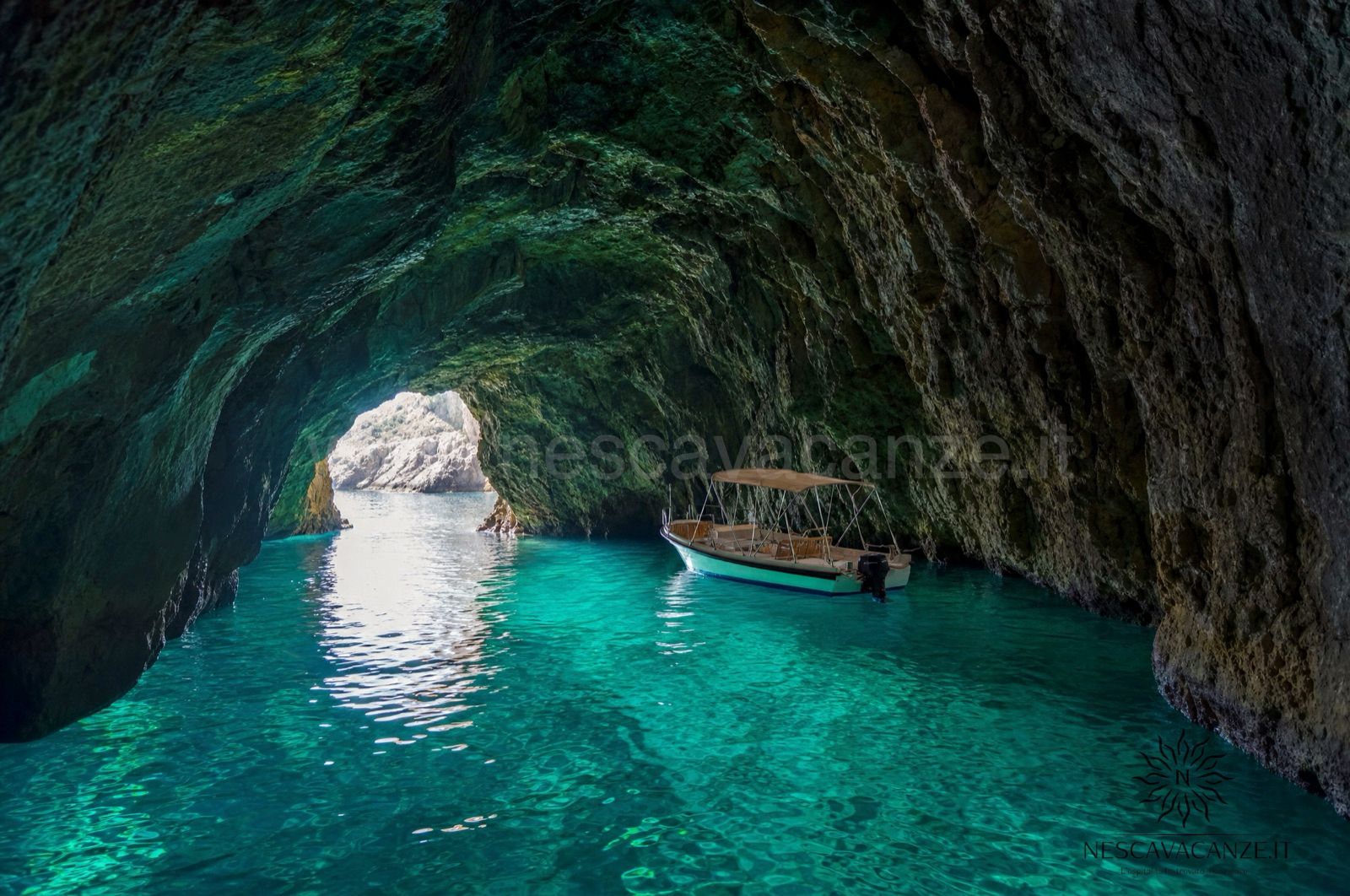 Interno di una grotta marina del Salento con acqua turchese illuminata e una piccola barca, vicino a Santa Maria di Leuca
