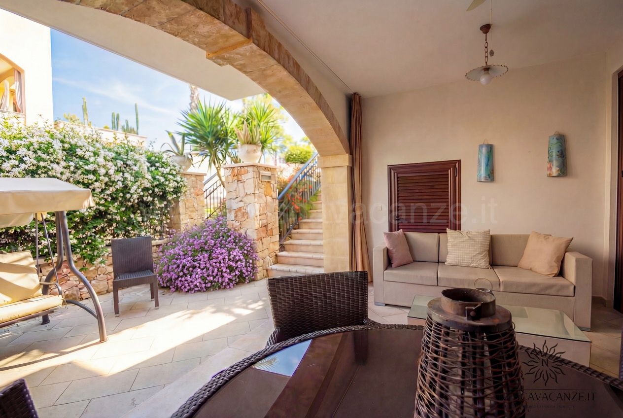Casa Pescoluse 6 - veranda coperta con divano beige, dondolo, arco in pietra e fiori viola