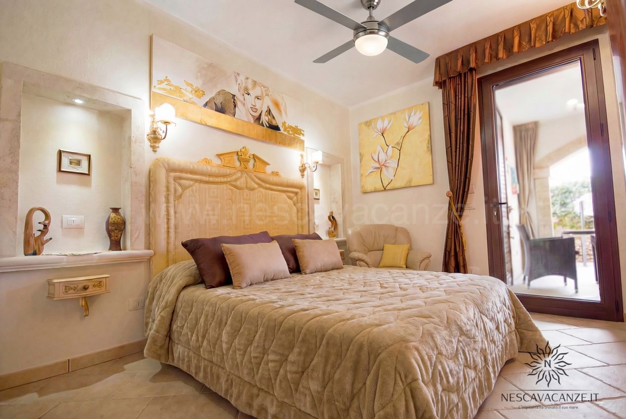 Casa Pescoluse 6 - camera matrimoniale con testiera dorata, quadri, poltrona e porta sul patio