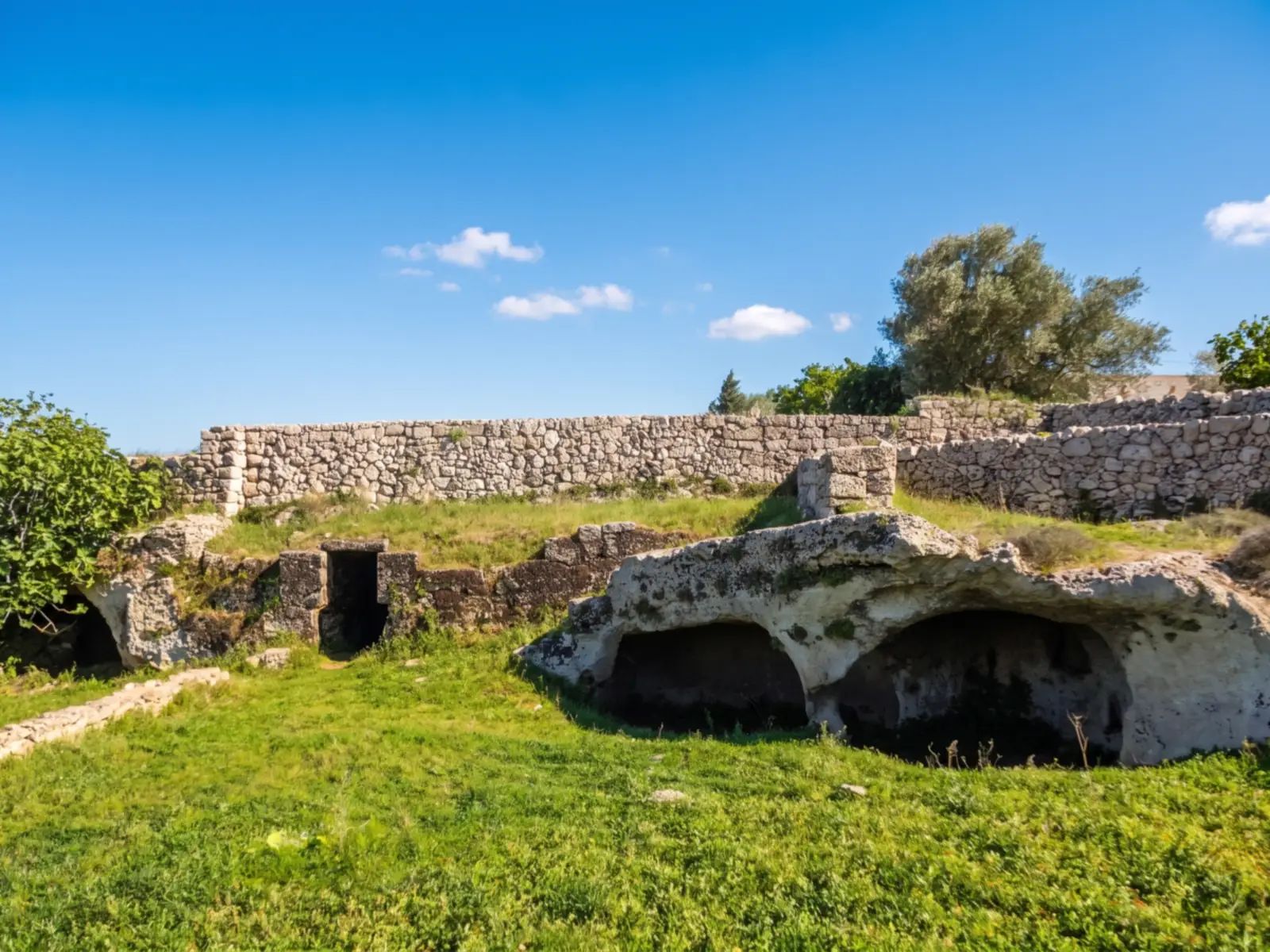 Le grotte scavate nella roccia del villaggio rupestre di Macurano, ad Alessano, sotto un muretto a secco e il prato