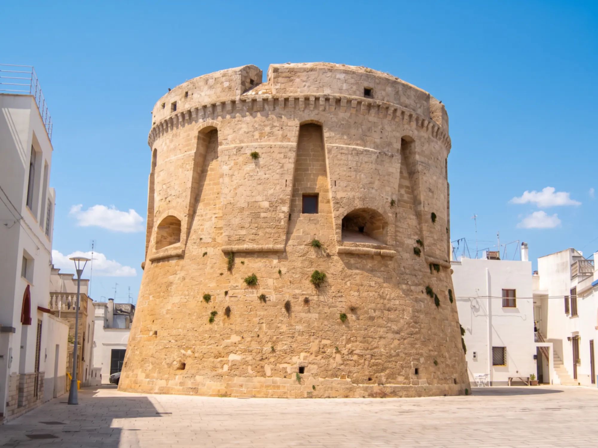La torre rotonda di Salignano, in pietra, al centro di una piazza tra case bianche