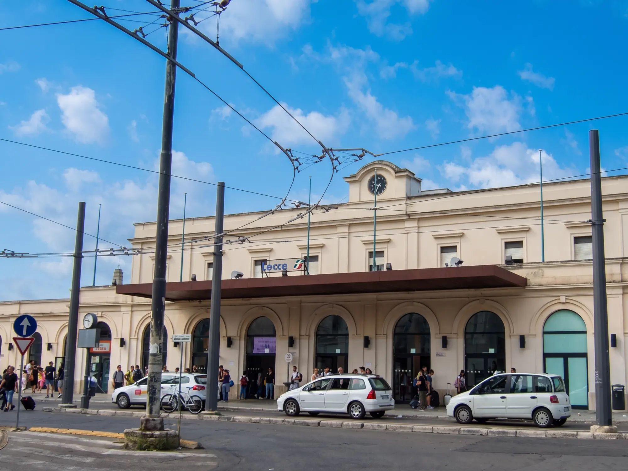 La facciata della stazione ferroviaria di Lecce, con i taxi davanti all'ingresso e i cavi della filovia