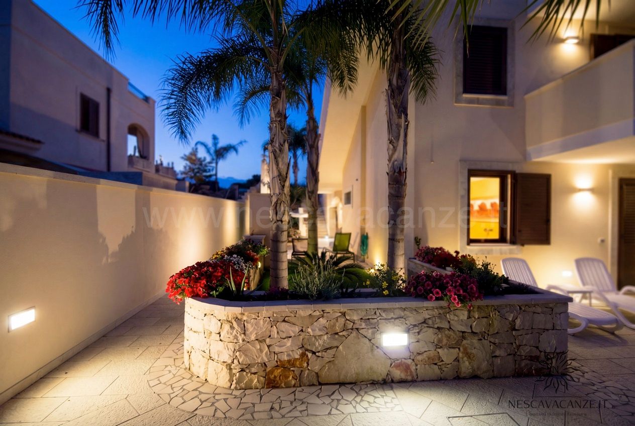 Casa Pescoluse 7 - cortile al crepuscolo con fioriera in pietra, palme e luci soffuse