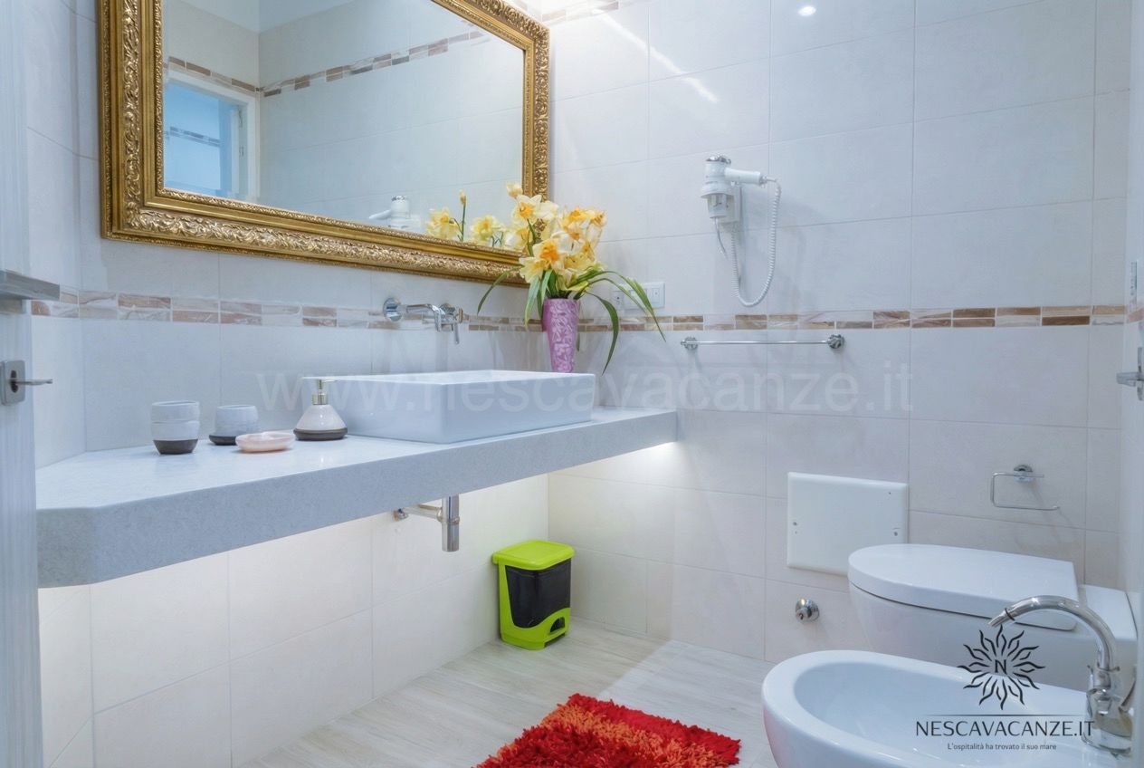 Casa Salento - bagno bianco con lavabo, specchio dorato, wc e bidet e tappeto rosso