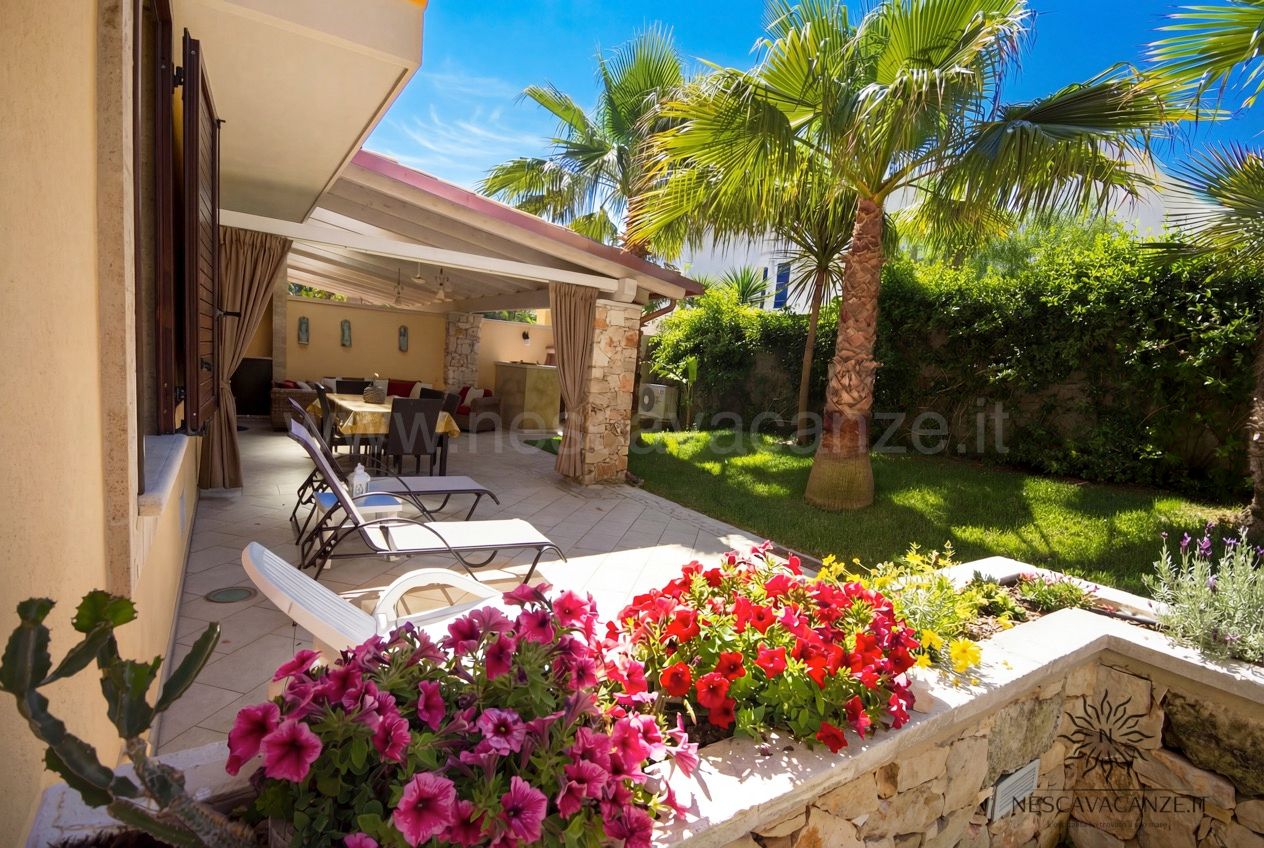 Casa Pescoluse 7 - terrazza coperta con tavolo da pranzo, lettini e giardino fiorito con palme