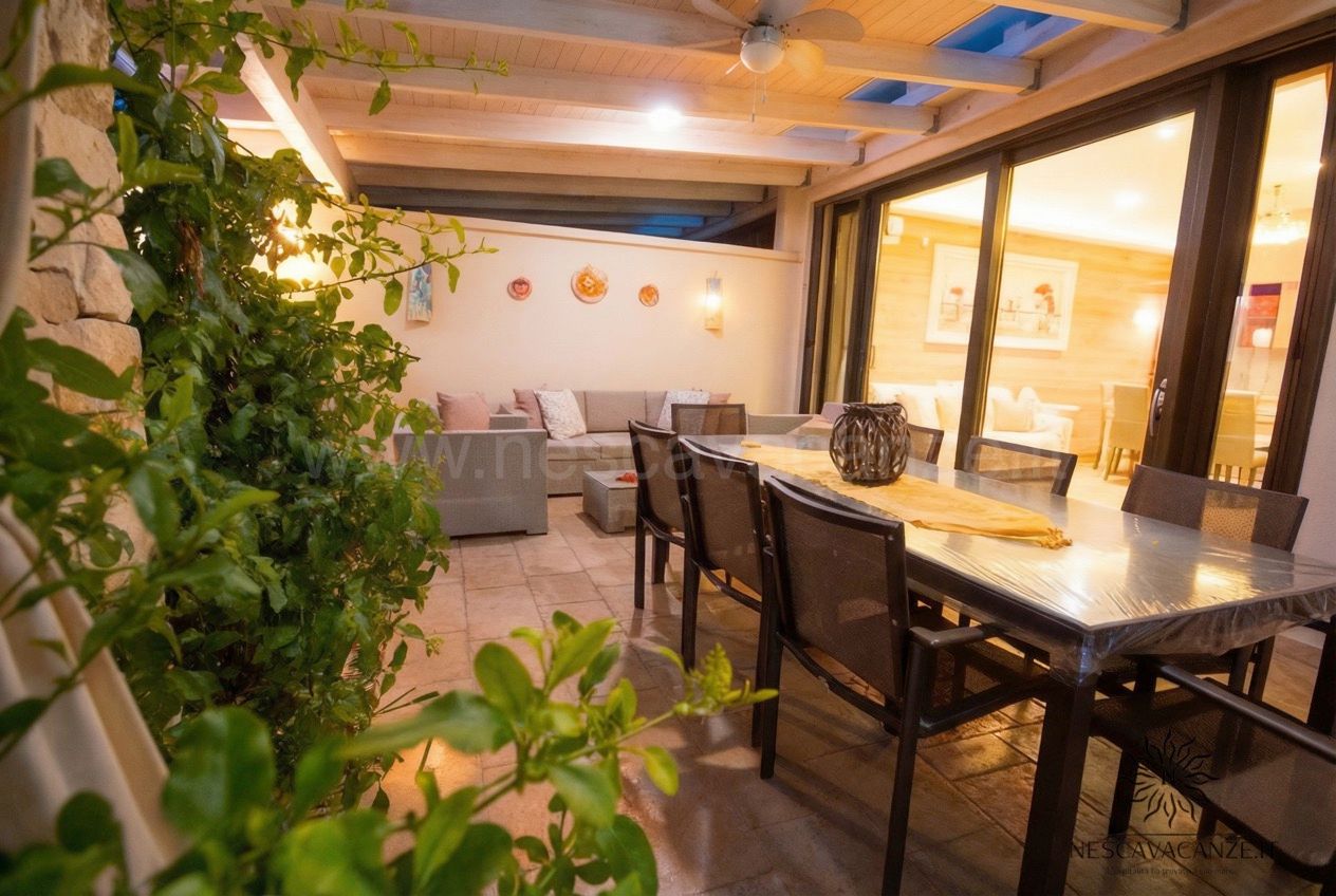 Casa Dune - patio esterno coperto con tavolo da pranzo, sedie, divani e piante verdi rampicanti sulla parete in pietra
