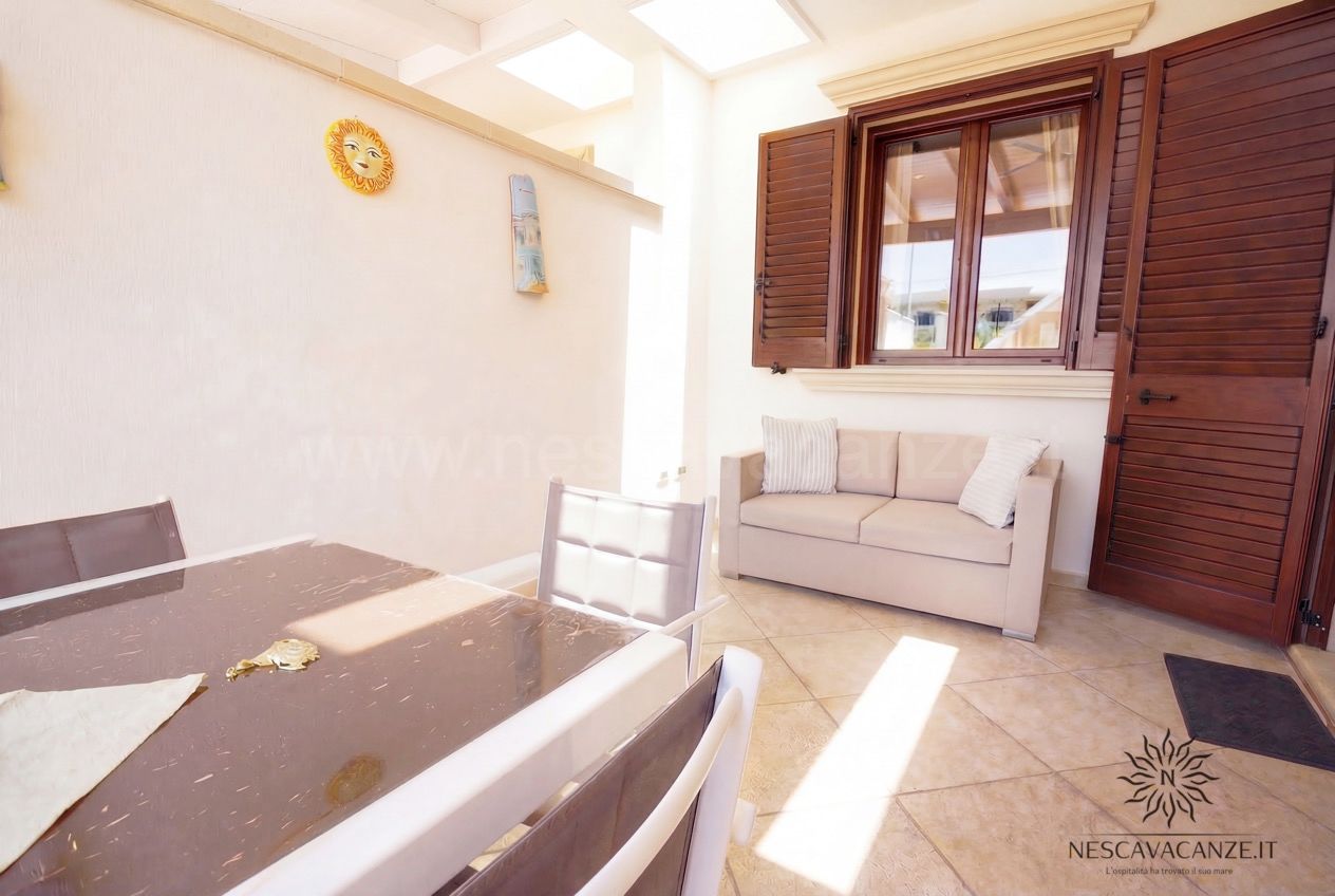 Casa Pescoluse 9 - veranda con tavolo in vetro, divano beige, persiane in legno e decori sole