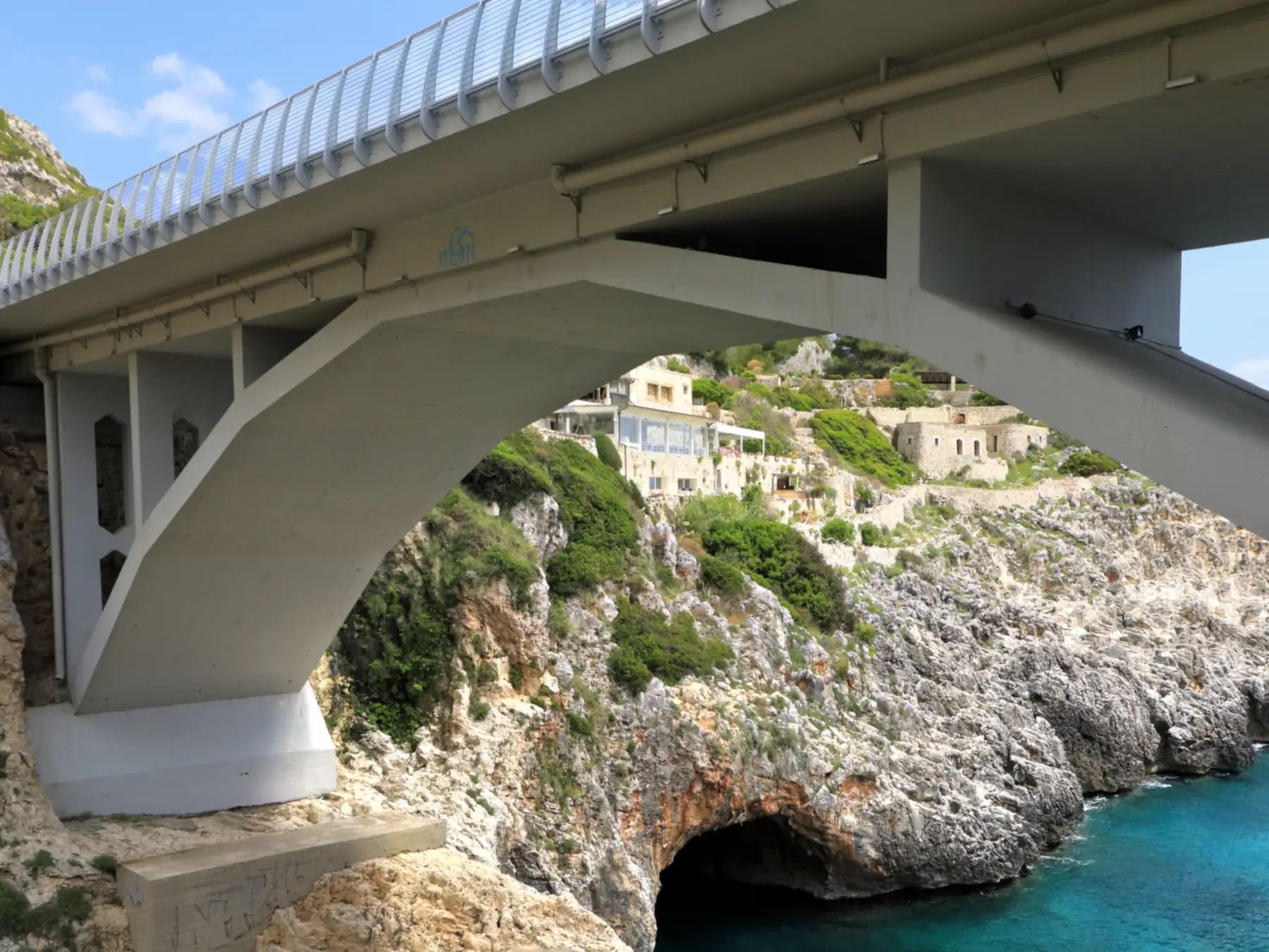 L'arco di cemento del Ponte del Ciolo visto dalla scalinata, sopra la grotta che si apre sull'acqua del canalone