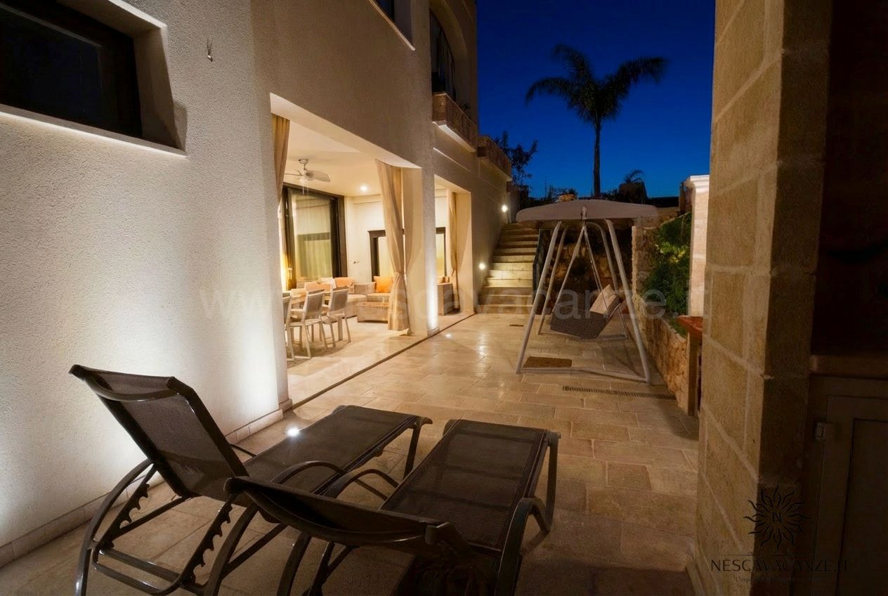 Casa Salento - patio notturno con lettini, dondolo e scala illuminata accanto al muro in pietra