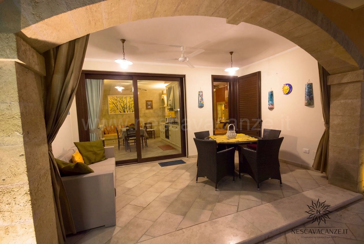 Casa Pescoluse 6 - veranda coperta serale con divano, tavolo in rattan e vista sulla cucina