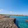 Scogliera bassa e mare verde-azzurro a Torre Pozzelle, con la torre sullo sfondo