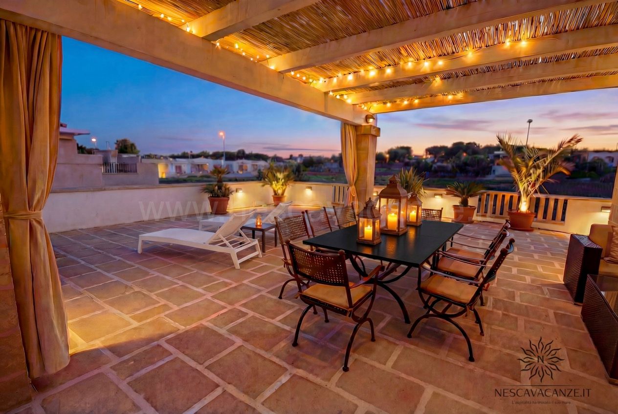 Casa Pescoluse 4 - terrazza al crepuscolo con pergolato luminoso, tavolo nero, sedie e lettino