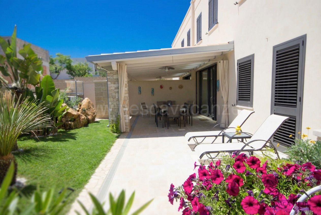Casa Dune - patio esterno con tavolo da pranzo coperto da pergola, lettini prendisole, prato verde e piante