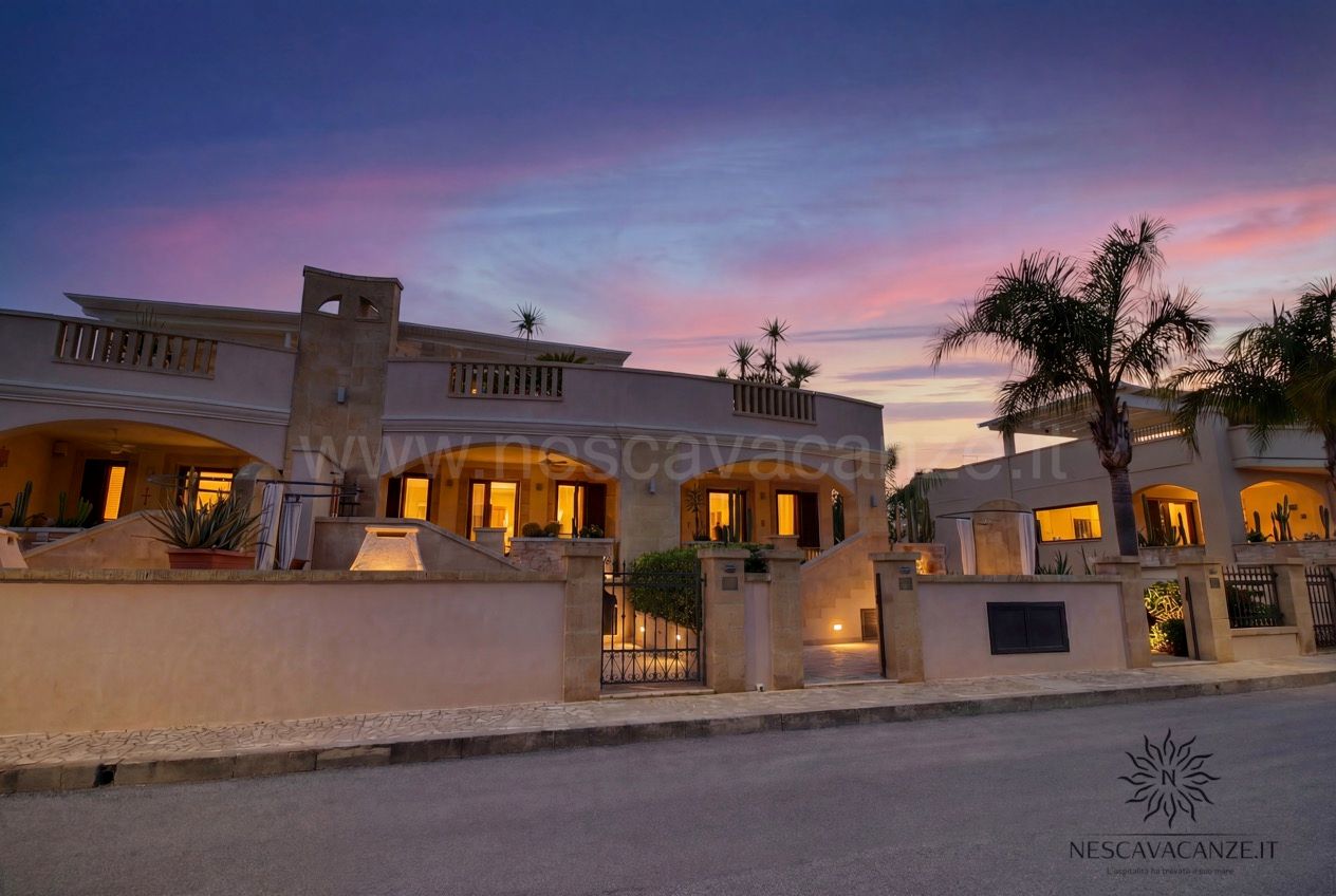 Casa Pescoluse 7 - facciata esterna al tramonto con finestre illuminate e cielo viola