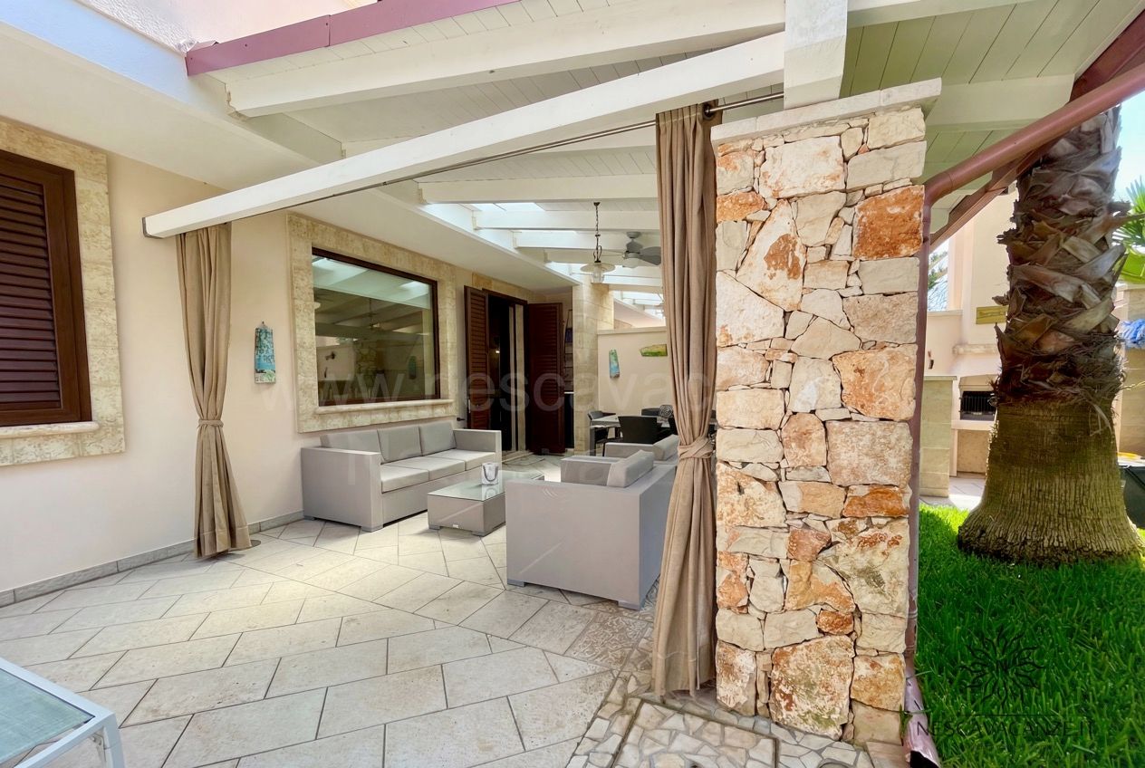 Casa Pescoluse 7 - salotto esterno coperto con divani grigi, pilastro in pietra e palma