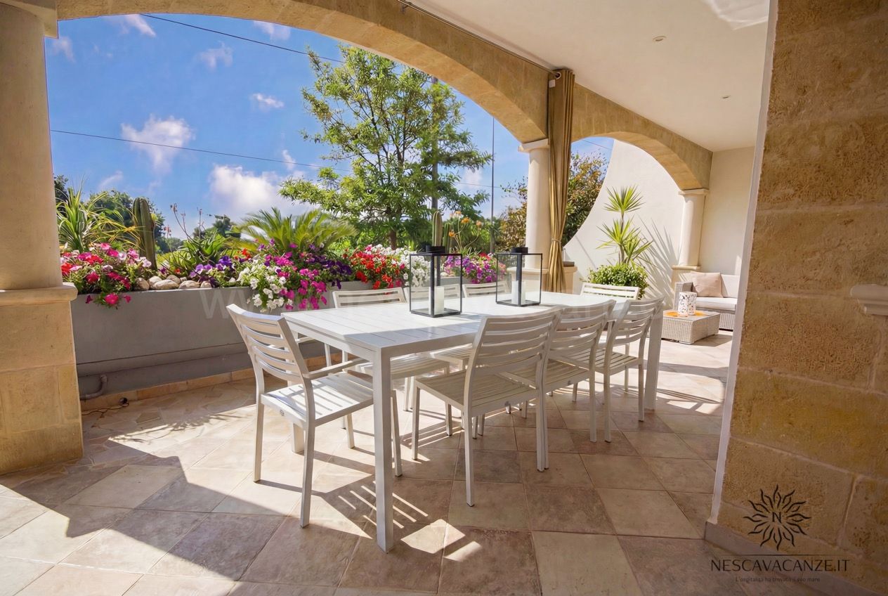 Casa Pescoluse 1 - veranda con tavolo e otto sedie bianche, fiori e vista sul giardino